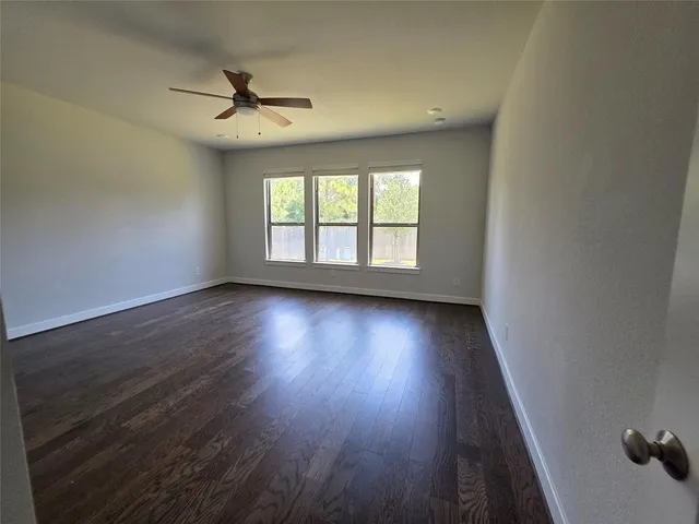 an empty room with wooden floor chandelier fan and windows