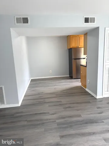 a view of empty room with wooden floor and kitchen
