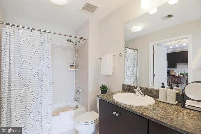 a bathroom with a granite countertop sink a toilet a mirror and shower