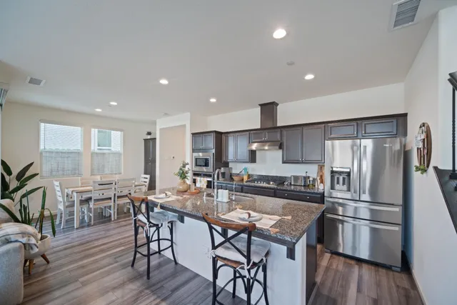 a kitchen with stainless steel appliances a dining table chairs stove refrigerator and wooden floor