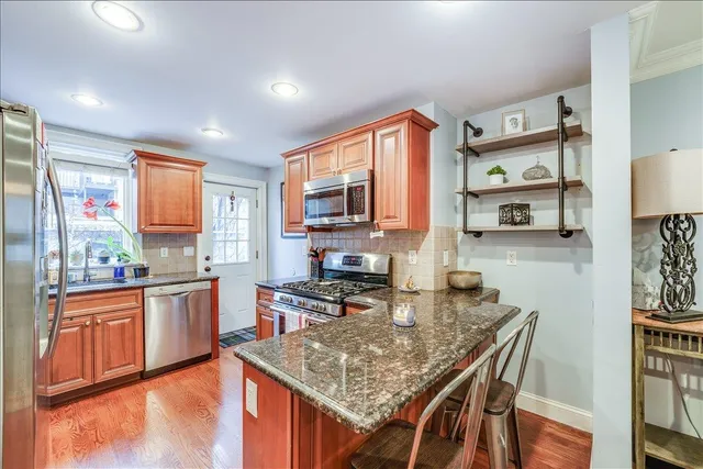 a kitchen with stainless steel appliances granite countertop a stove top oven a sink dishwasher a dining table and chairs with wooden floor