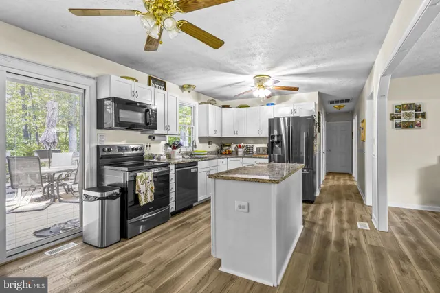 a kitchen with kitchen island granite countertop a stove top oven a sink dishwasher a refrigerator and a dining table with wooden floor