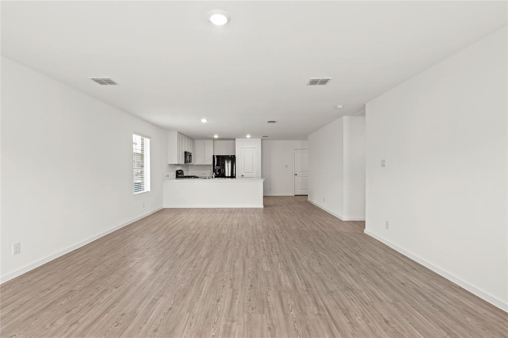 1138 Barbary Flds Street Forney, TX 75126 - Photo 7 of 25 Spacious open-concept interior featuring light wood-finish flooring, recessed lighting, and a kitchen with white cabinetry, dark countertops, and black appliances