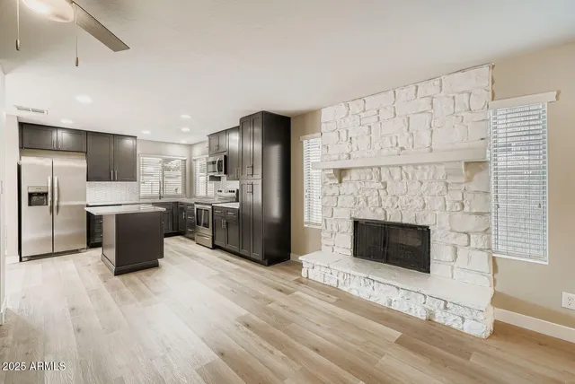 a kitchen with stainless steel appliances kitchen island granite countertop a refrigerator a fireplace with white cabinets