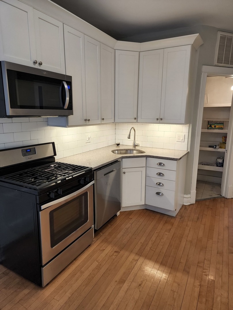 5225 North Clark Street, Unit 2 Chicago, IL 60640 - Photo 8 of 21 a kitchen with stainless steel appliances kitchen island granite countertop a stove a sink and a microwave