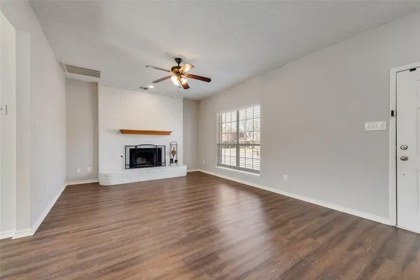 a view of an empty room with wooden floor fireplace and a window