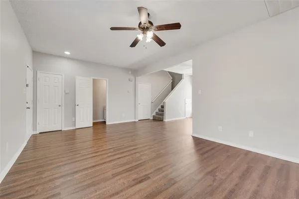 a view of an empty room with wooden floor and a ceiling fan