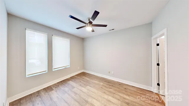 an empty room with wooden floor ceiling fan and windows