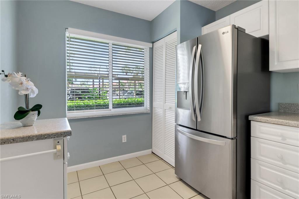 4556 Andover Way, Unit E106 Naples, FL 34112 - Photo 11 of 40 Kitchen with white cabinets, stainless steel fridge, light tile patterned floors, and light stone counters