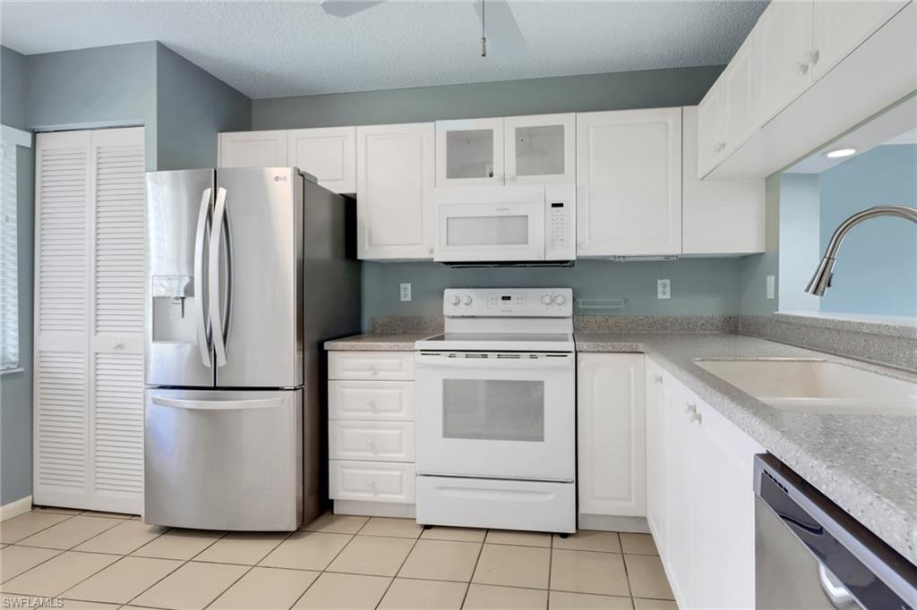 4556 Andover Way, Unit E106 Naples, FL 34112 - Photo 12 of 40 Kitchen featuring stainless steel appliances, glass fronted cabinets, white cabinetry, light tile patterned floors, and a textured ceiling