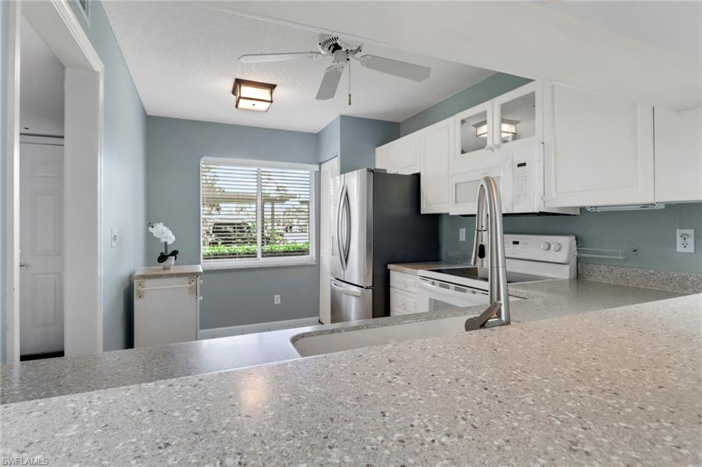 4556 Andover Way, Unit E106 Naples, FL 34112 - Photo 13 of 40 Kitchen featuring white cabinets, glass fronted cabinets, light stone counters, a ceiling fan, and white appliances