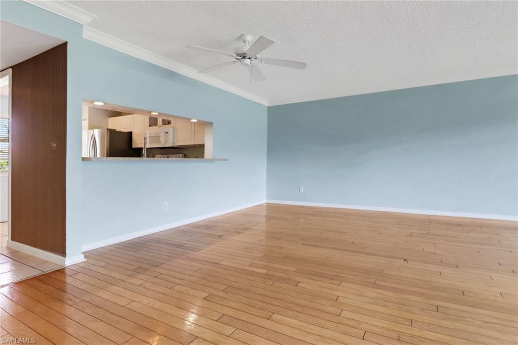 4556 Andover Way, Unit E106 Naples, FL 34112 - Photo 14 of 40 Unfurnished living room featuring crown molding, light wood-style flooring, a ceiling fan, and a textured ceiling