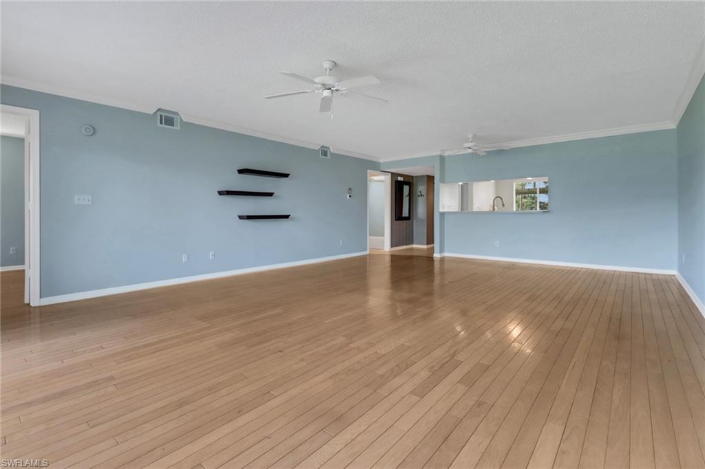 4556 Andover Way, Unit E106 Naples, FL 34112 - Photo 18 of 40 Unfurnished living room with light wood-style flooring, a ceiling fan, crown molding, and a textured ceiling