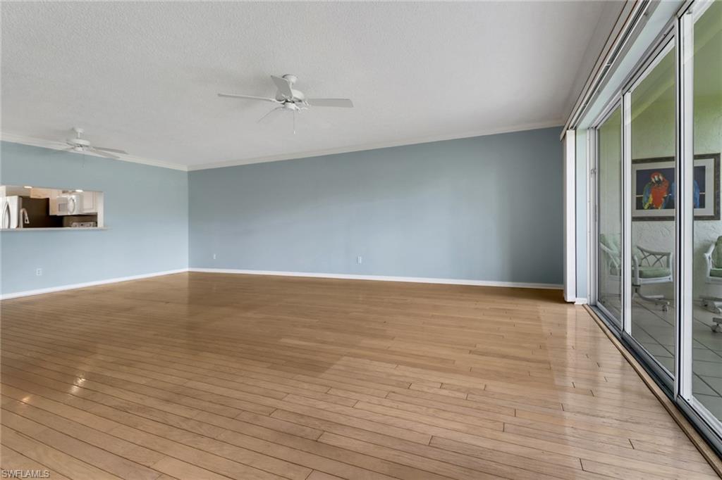 4556 Andover Way, Unit E106 Naples, FL 34112 - Photo 7 of 40 Unfurnished living room featuring a ceiling fan, light wood-style flooring, a textured ceiling, and ornamental molding