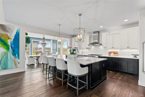 a kitchen with stainless steel appliances granite countertop a stove a refrigerator a kitchen island a dining table and chairs with wooden floor