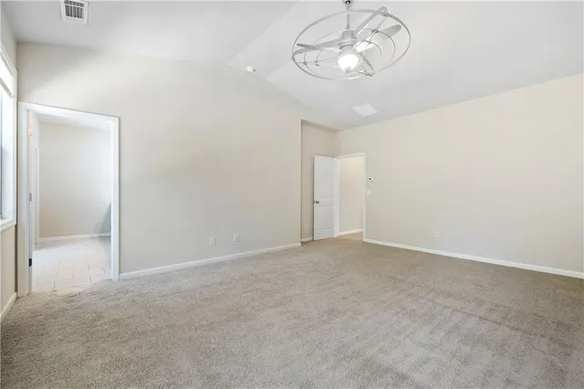 en empty room with a chandelier fan and kitchen view