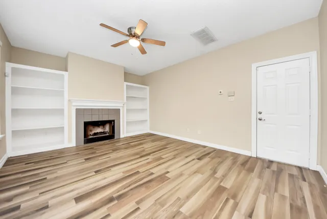 a view of an empty room with wooden floor fireplace and a window
