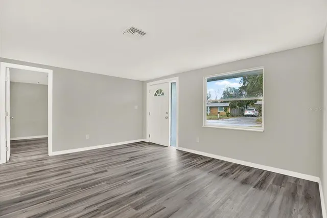 a view of an empty room with wooden floor and a window