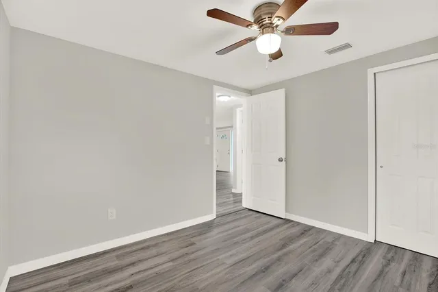 an empty room with wooden floor ceiling fan and window