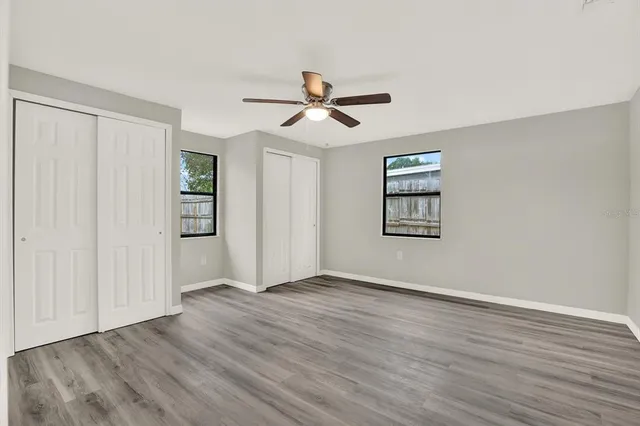 an empty room with wooden floor ceiling fan and windows