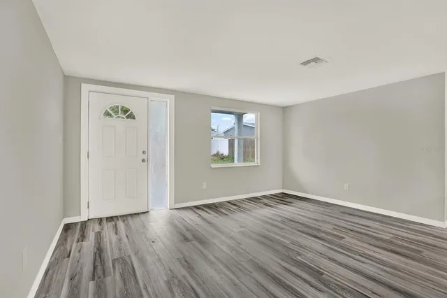 a view of an empty room with wooden floor and a window