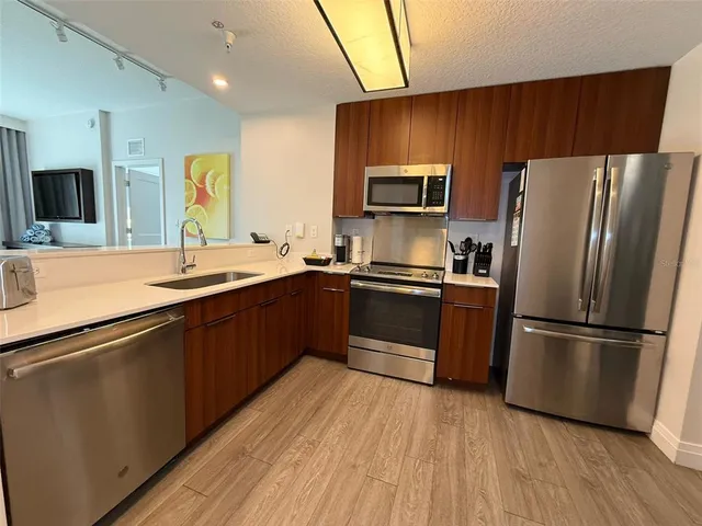 a kitchen with kitchen island granite countertop wooden floors stainless steel appliances a sink and a refrigerator