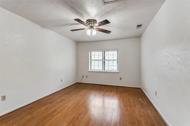 an empty room with wooden floor a ceiling fan and windows