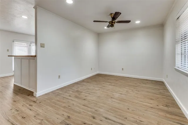 an empty room with wooden floor chandelier fan and windows