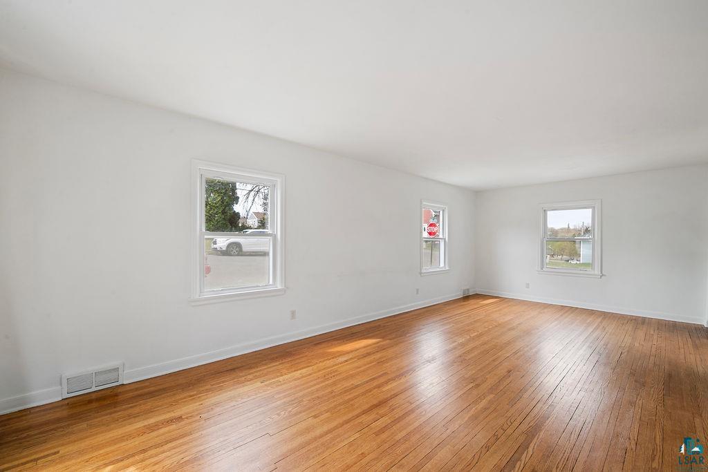 122 3rd Street Cloquet, MN 55720 - Photo 4 of 42 Spacious room featuring hardwood flooring, crisp white walls, multiple windows with white trim, and baseboard registers