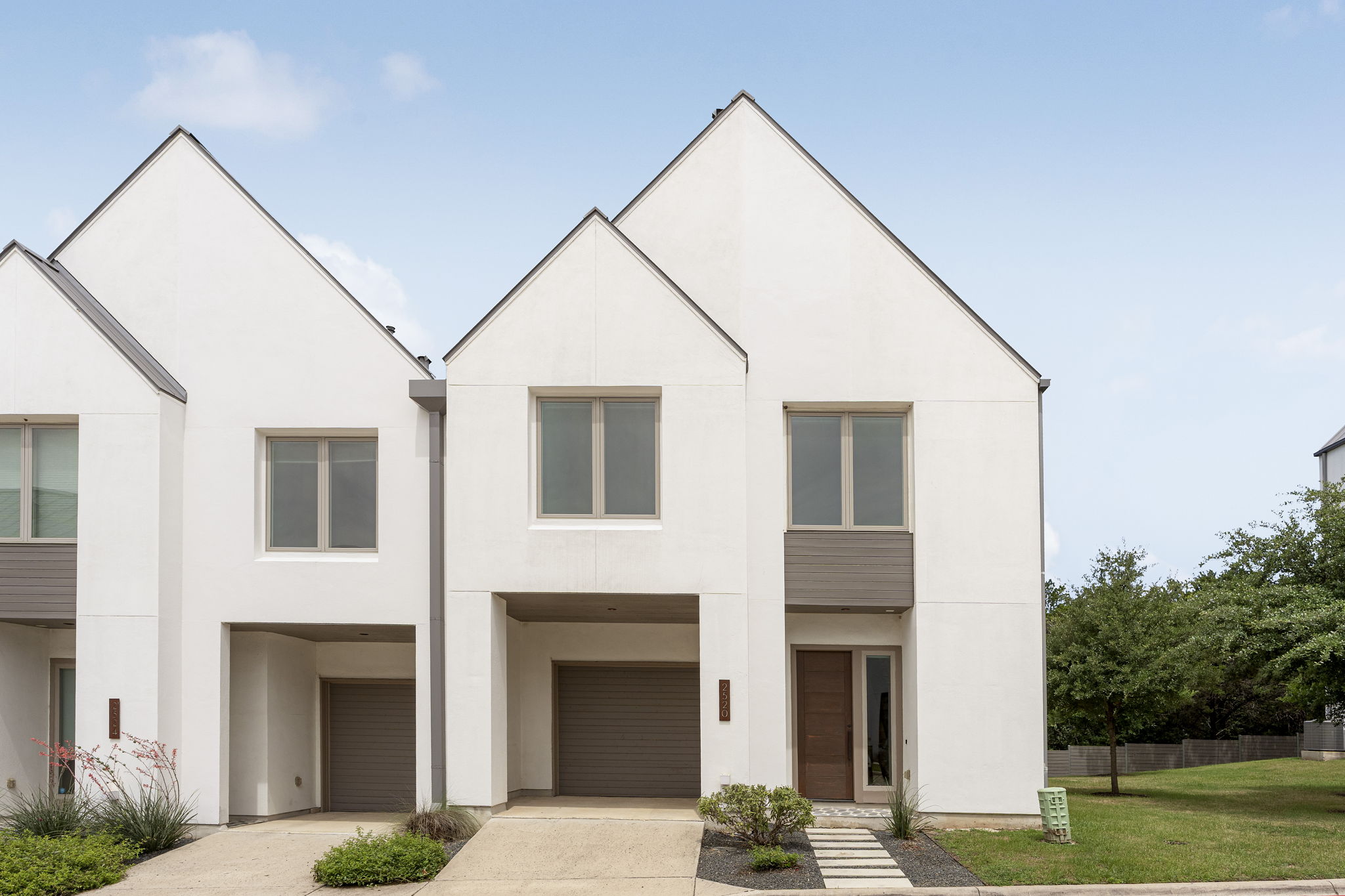 2520 Sutherland Street Austin, TX 78746 - Photo 1 of 26 Modern townhome showcases a crisp white facade with a distinct gabled roofline and an integrated garage entrance.