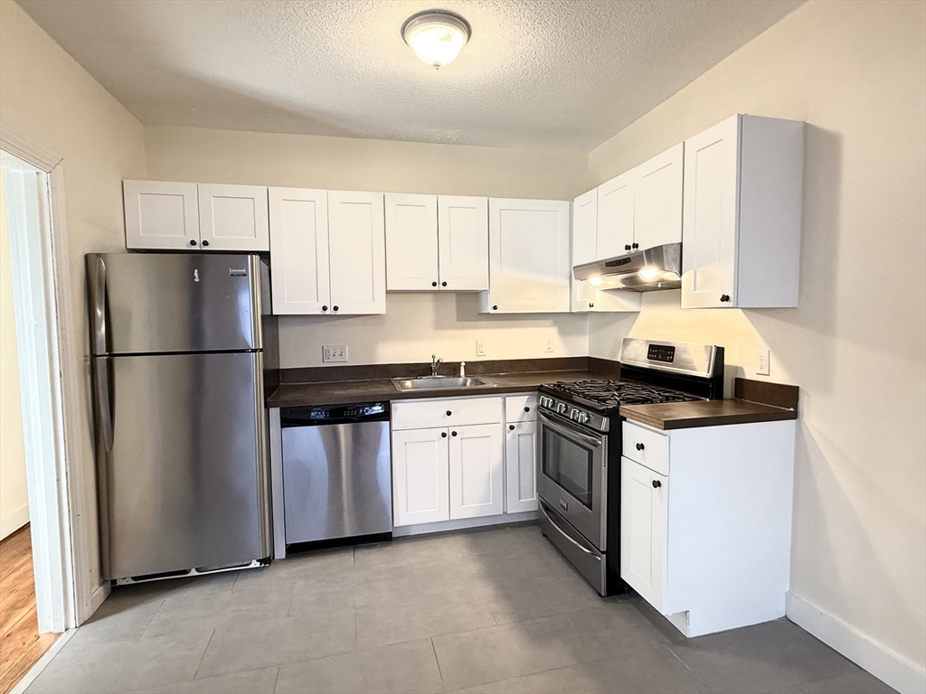 18 Roberts Street, Unit 1 Brookline, MA 02445 - Photo 4 of 10 a kitchen with stainless steel appliances granite countertop a refrigerator stove a sink and a granite counter tops