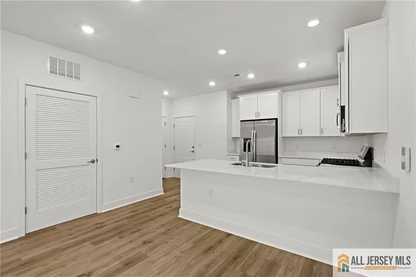 a large kitchen with stainless steel appliances granite countertop a stove a sink a refrigerator and white cabinets with wooden floor