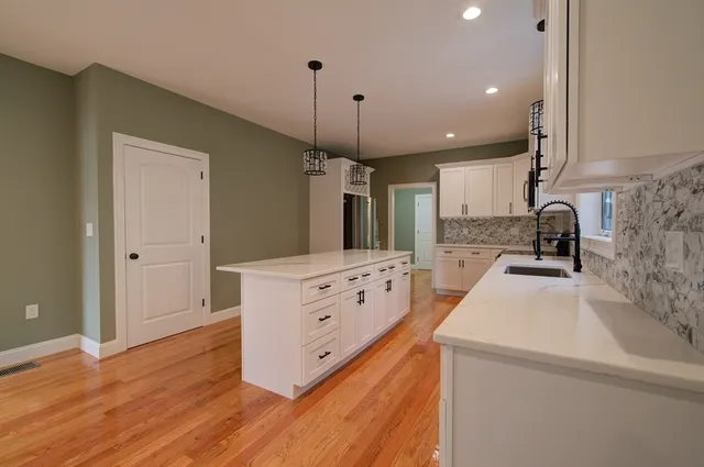 a kitchen with granite countertop a sink stove a refrigerator and white cabinets with wooden floor