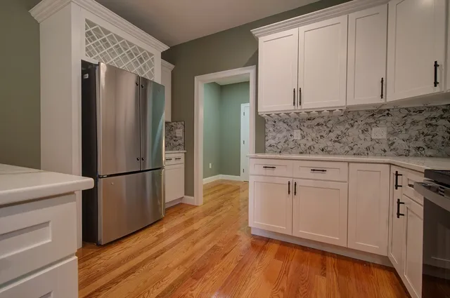 a kitchen with stainless steel appliances granite countertop a refrigerator stove and white cabinets with wooden floor
