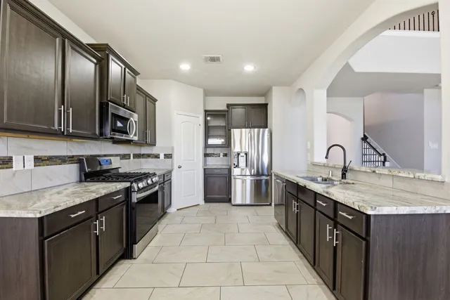 a kitchen with stainless steel appliances granite countertop a stove a sink dishwasher a refrigerator and a microwave oven with wooden cabinets