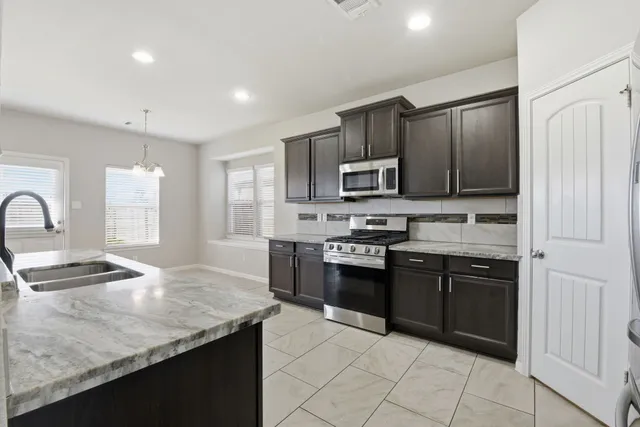 a large kitchen with kitchen island granite countertop a stove top oven a sink a counter space cabinets and a window