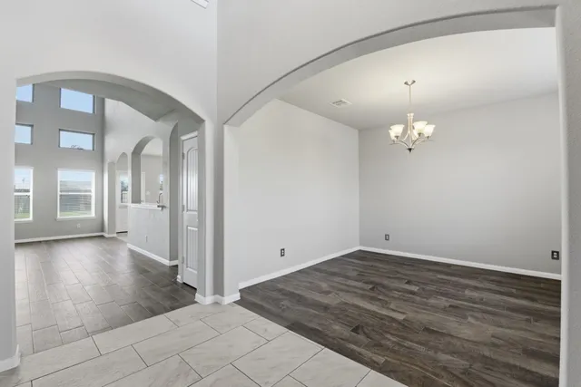 an empty room with wooden floor chandelier and windows