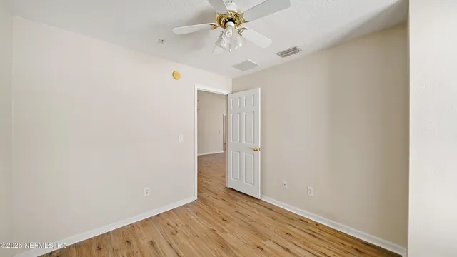 a view of an empty room with chandelier fan and wooden floor