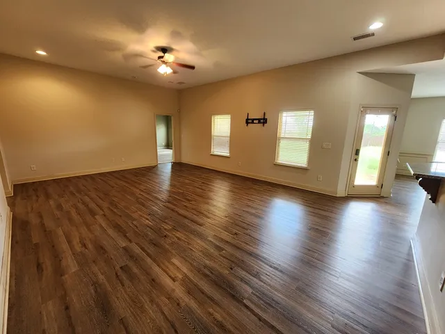 a view of an empty room with wooden floor and a kitchen