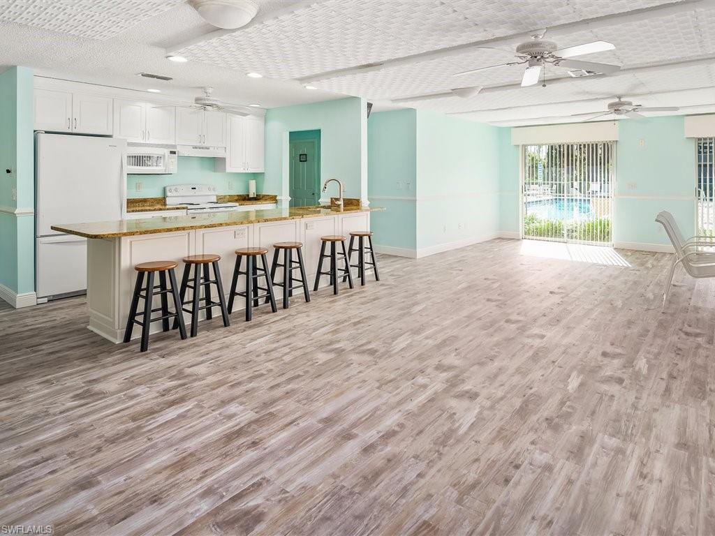 3012 Sandpiper Bay Circle, Unit D301 Naples, FL 34112 - Photo 21 of 23 a open kitchen with kitchen island a stove a refrigerator a sink dishwasher with a dining table and chairs with wooden floor