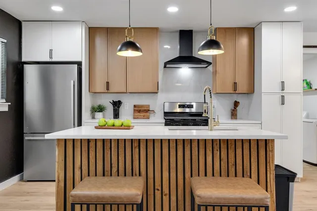 a kitchen with stainless steel appliances granite countertop a refrigerator a sink dishwasher a stove white cabinets and chairs with wooden floor