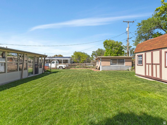 1502 North 475 West Sunset, UT 84015 - Photo 21 of 23 Expansive grass lawn bordered by a screened enclosure and a detached storage shed with a shingled roof