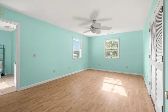 an empty room with wooden floor ceiling fan and windows