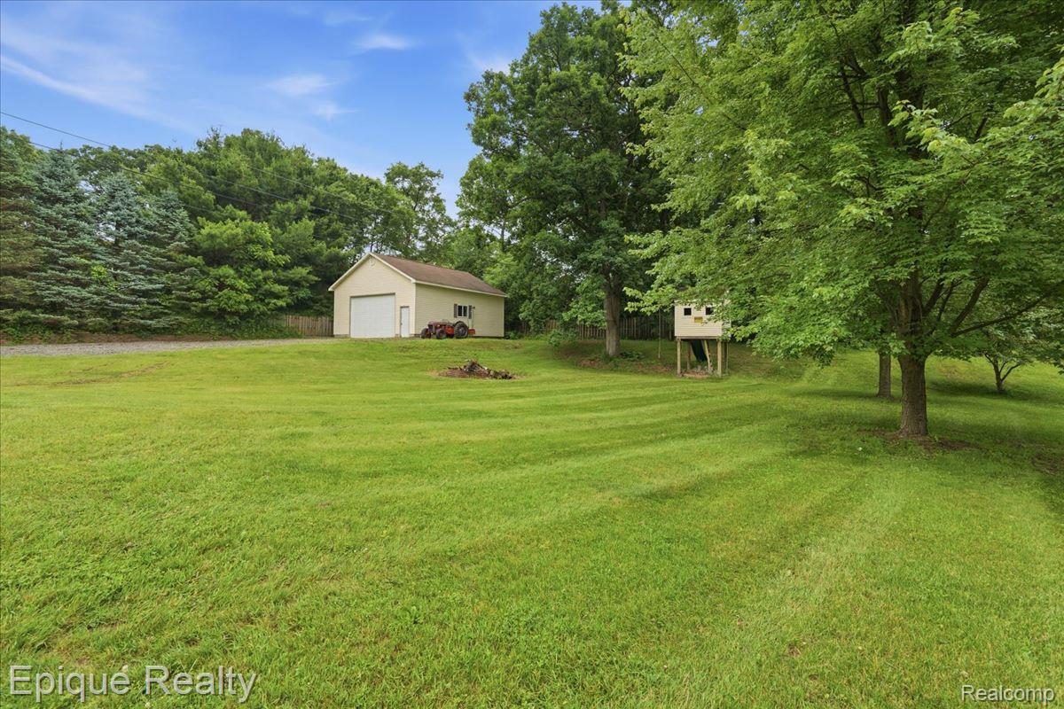 1221 Rhodes Road Lake Orion, MI 48360 - Photo 50 of 72 Expansive lawn area featuring a detached garage with a white overhead door, mature trees, and a visible play structure