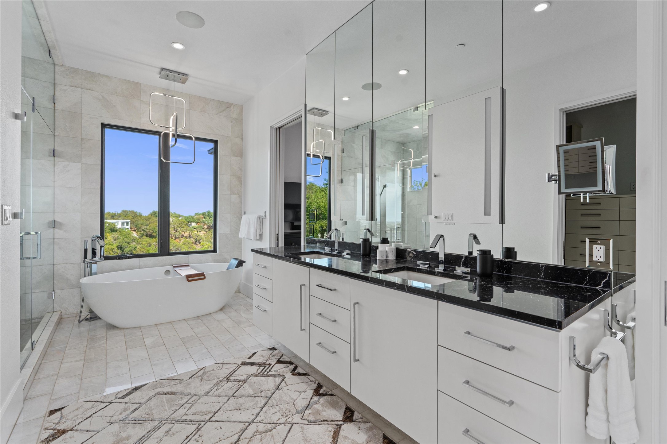 1500 The High Road Austin, TX 78746 - Photo 21 of 40 Primary Bathroom with Freestanding soaking tub with a scenic backdrop, complemented by a dual vanity featuring black stone countertops