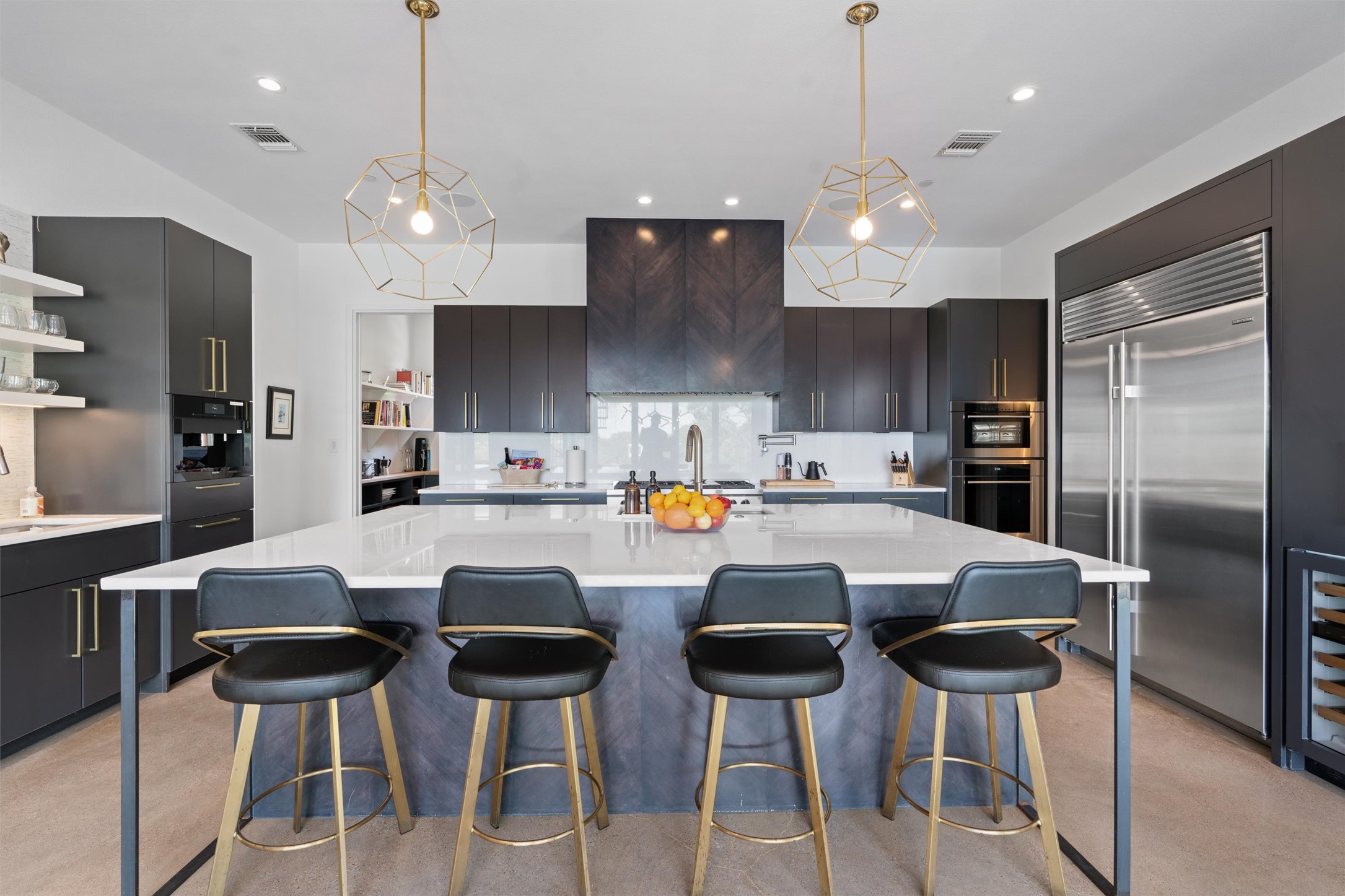 1500 The High Road Austin, TX 78746 - Photo 10 of 40 Contemporary kitchen featuring a large central island with seating, dark flat-panel cabinetry, stainless steel appliances including a built-in refrigerator and oven, and geometric pendant lighting fixtures