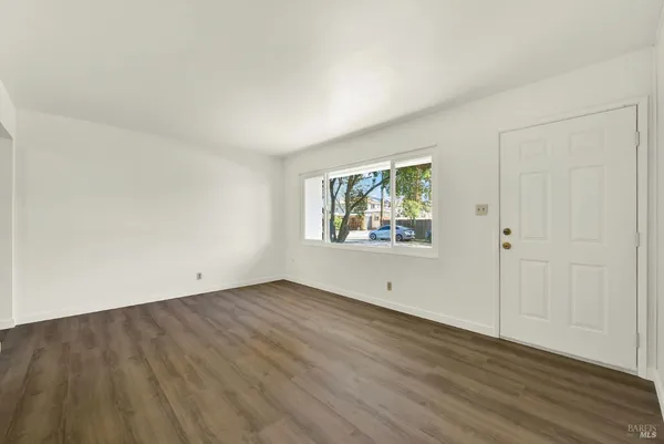 a view of an empty room with wooden floor and a window