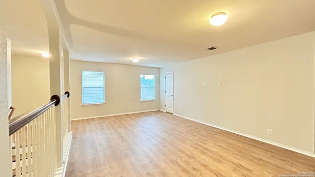 an empty room with wooden floor fan and windows