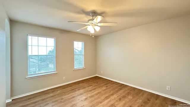 an empty room with wooden floor chandelier fan and windows