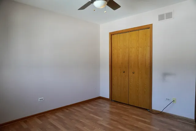 a view of an empty room with wooden floor and a chandelier fan